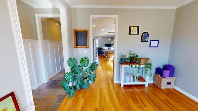 corridor with wood finished floors, ornamental molding, and wainscoting