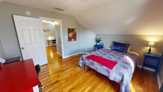 bedroom with light wood-type flooring, visible vents, baseboards, and vaulted ceiling