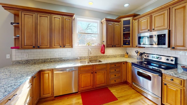 kitchen featuring light wood finished floors, light stone countertops, ornamental molding, appliances with stainless steel finishes, and a sink