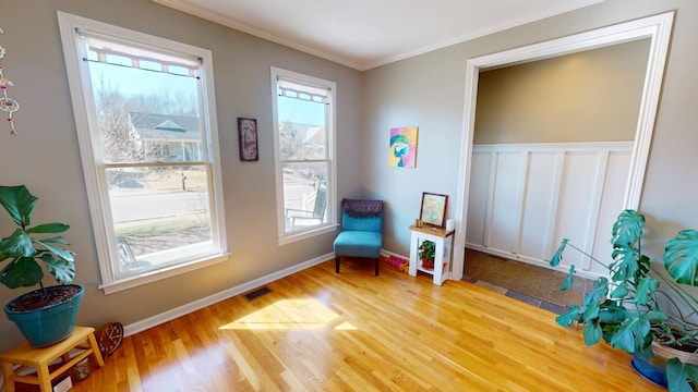 sitting room with visible vents, a wainscoted wall, wood finished floors, crown molding, and baseboards