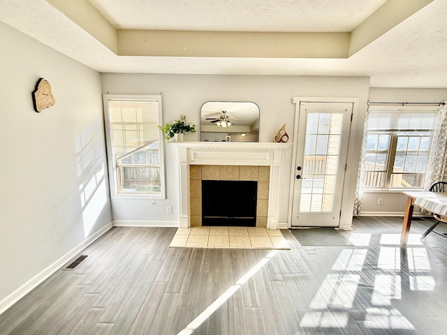 unfurnished living room with visible vents, a textured ceiling, wood finished floors, a tile fireplace, and baseboards