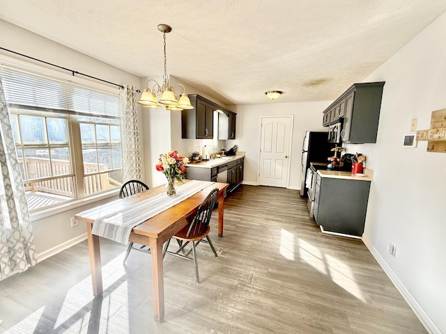 dining area featuring baseboards, a textured ceiling, light wood-type flooring, and a notable chandelier