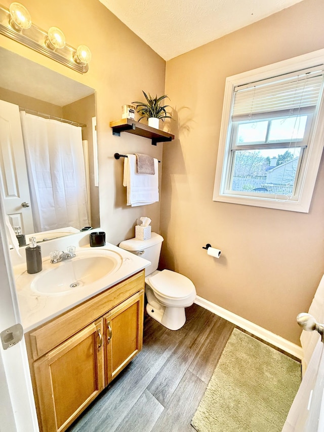 bathroom with a textured ceiling, toilet, wood finished floors, vanity, and baseboards