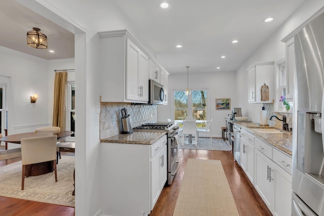 kitchen featuring dark wood finished floors, decorative backsplash, appliances with stainless steel finishes, a sink, and light stone countertops