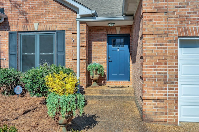 view of exterior entry with brick siding, an attached garage, and a shingled roof