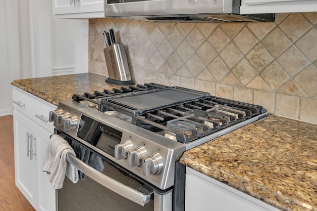 kitchen with white cabinets, dark stone countertops, stainless steel range with gas stovetop, and decorative backsplash