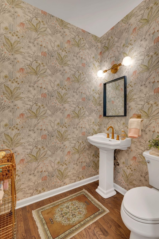 half bathroom with wood finished floors, toilet, baseboards, and wallpapered walls