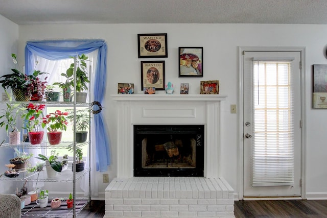 living room featuring a brick fireplace, a textured ceiling, baseboards, and wood finished floors