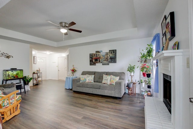 living area with a tray ceiling, a brick fireplace, ceiling fan, and wood finished floors