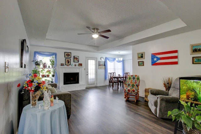 living room with baseboards, a raised ceiling, a ceiling fan, dark wood-style flooring, and a brick fireplace