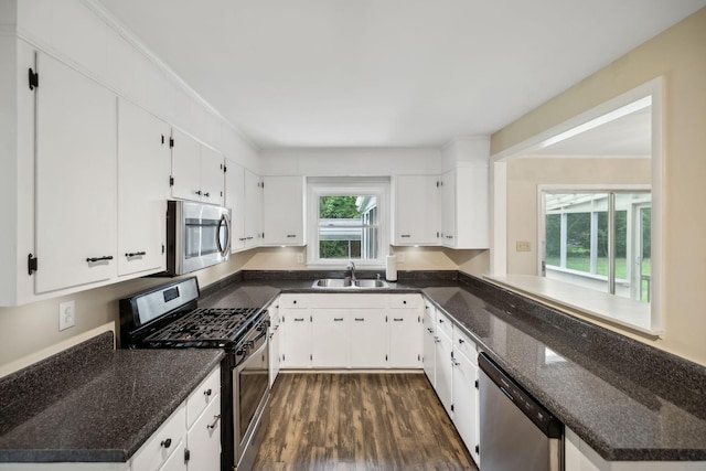 kitchen with stainless steel appliances, a sink, white cabinets, dark stone countertops, and dark wood finished floors