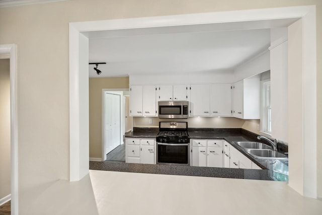 kitchen with dark countertops, appliances with stainless steel finishes, a sink, white cabinetry, and track lighting