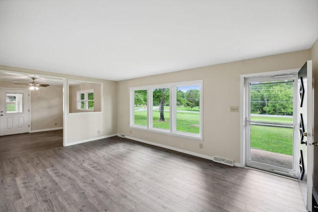 unfurnished living room with a wealth of natural light, visible vents, baseboards, and wood finished floors