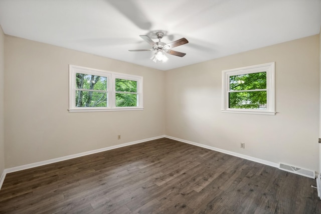 unfurnished room featuring a wealth of natural light, dark wood-type flooring, visible vents, and baseboards