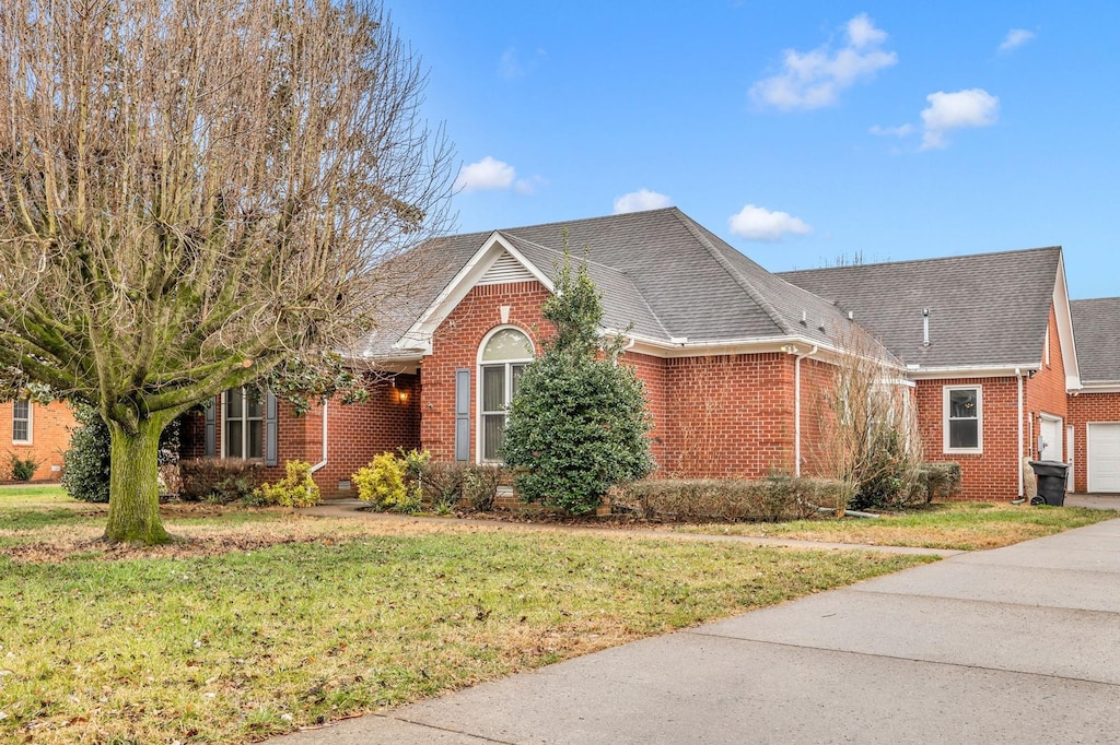 view of front facade featuring a shingled roof, a front yard, and brick siding