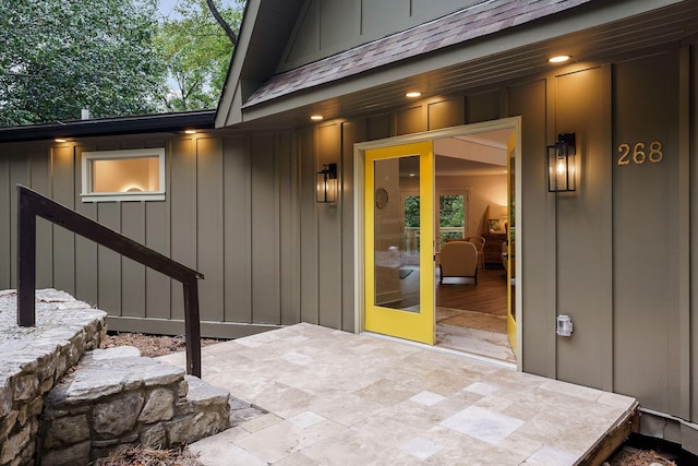 property entrance featuring roof with shingles, board and batten siding, and a patio area