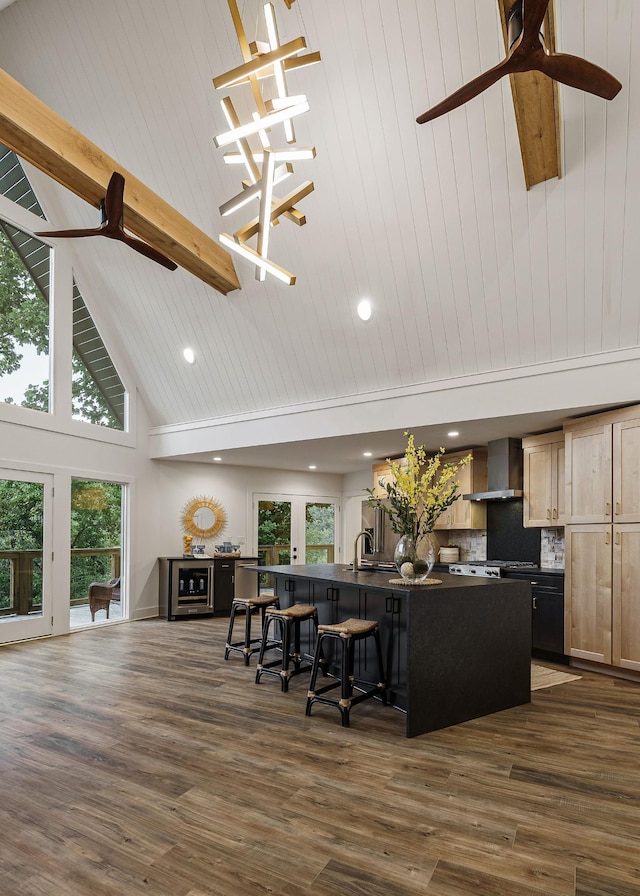 kitchen featuring high vaulted ceiling, dark countertops, a kitchen island with sink, and wall chimney exhaust hood