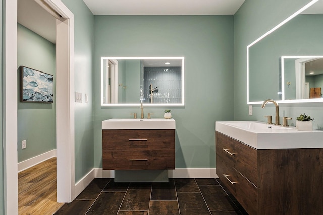 full bathroom featuring wood finished floors, two vanities, a sink, and baseboards