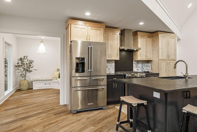 kitchen featuring high end fridge, light brown cabinets, wall chimney range hood, and dark countertops