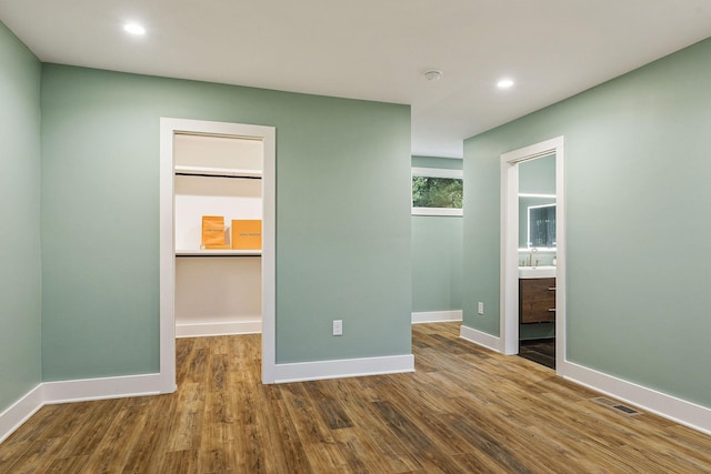 unfurnished bedroom with baseboards, a spacious closet, visible vents, and wood finished floors