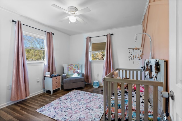 bedroom with dark wood-style floors, baseboards, a ceiling fan, and a nursery area