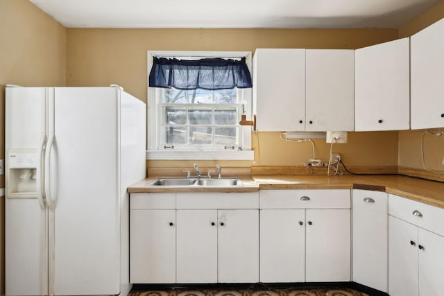 kitchen with white refrigerator with ice dispenser, white cabinetry, and a sink