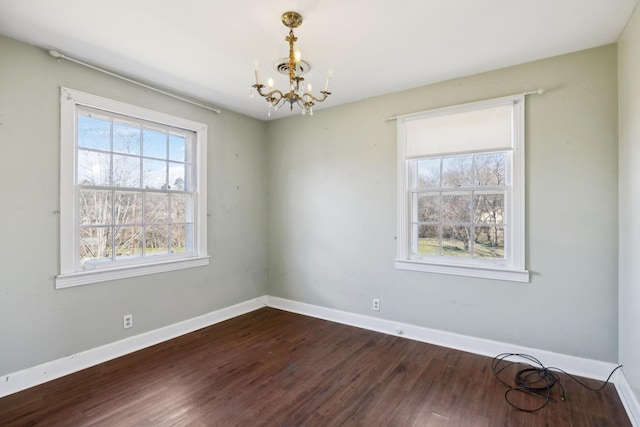 spare room with a chandelier, dark wood finished floors, and baseboards