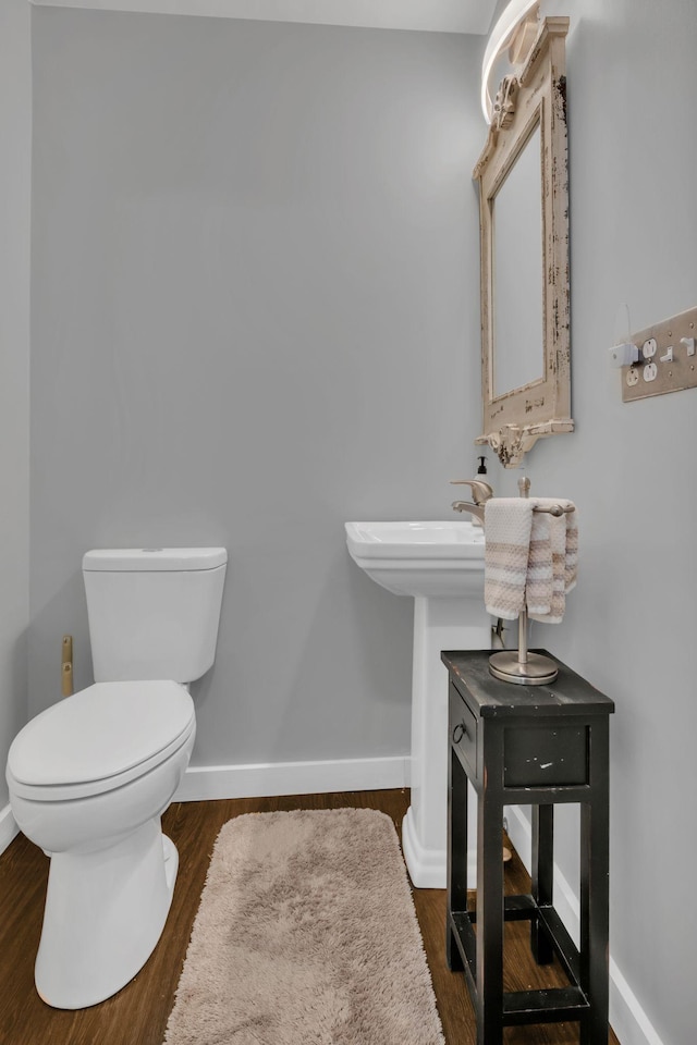 half bathroom with toilet, baseboards, and wood finished floors