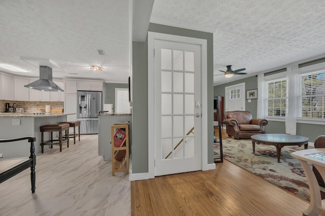 interior space with a textured ceiling, visible vents, a ceiling fan, light wood-style floors, and ornamental molding