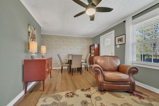 living area with a textured ceiling, wood finished floors, baseboards, ornamental molding, and wallpapered walls