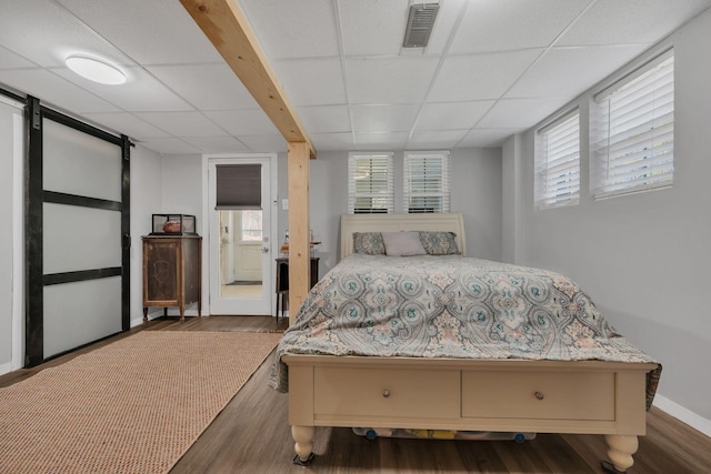 bedroom featuring a barn door, a paneled ceiling, wood finished floors, visible vents, and multiple windows