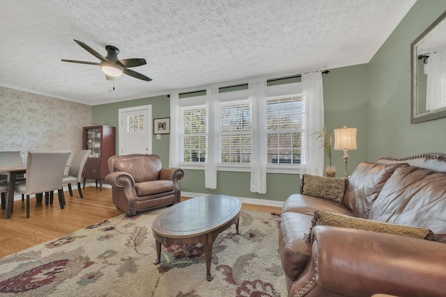 living room featuring ornamental molding, a ceiling fan, baseboards, and wood finished floors