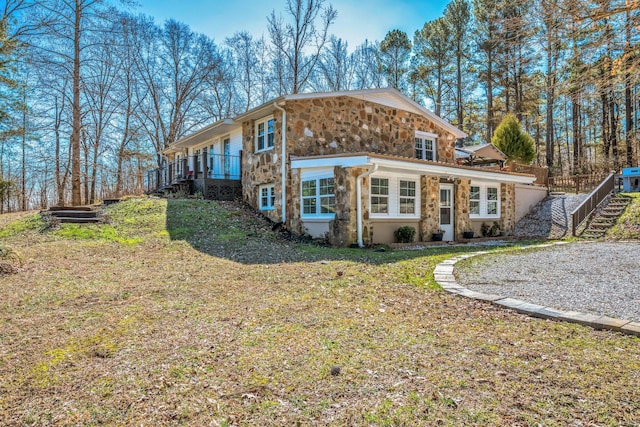 rear view of property with stairs, stone siding, and a yard