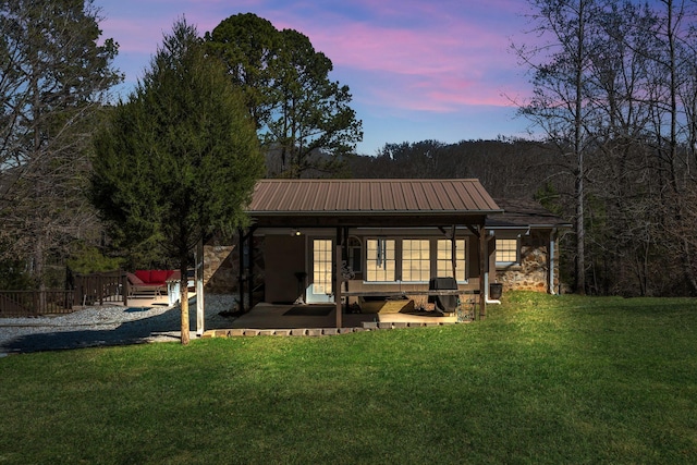 back of property with stone siding, metal roof, a patio, and a lawn