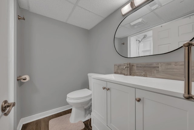 bathroom featuring baseboards, a drop ceiling, toilet, wood finished floors, and vanity