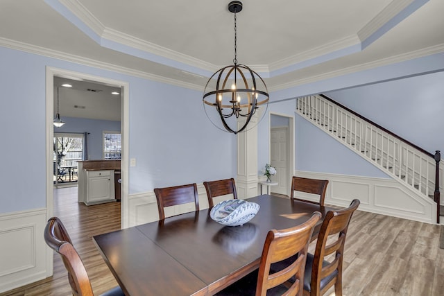 dining area featuring wood finished floors, a raised ceiling, a wainscoted wall, and stairs