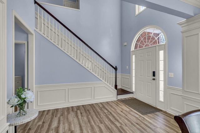 entrance foyer with stairs, a wainscoted wall, a decorative wall, and wood finished floors