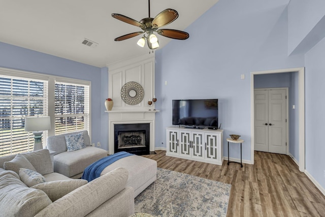 living room featuring a large fireplace, visible vents, baseboards, a ceiling fan, and wood finished floors