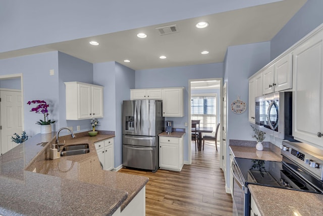 kitchen with stainless steel appliances, visible vents, a sink, wood finished floors, and a peninsula