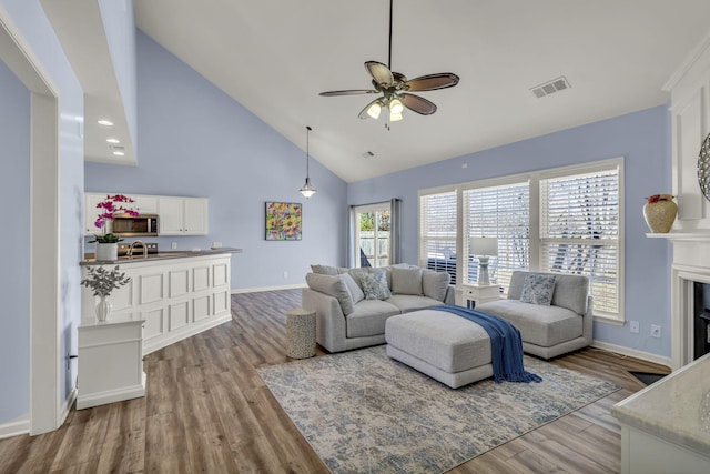 living room with a fireplace, visible vents, wood finished floors, high vaulted ceiling, and baseboards