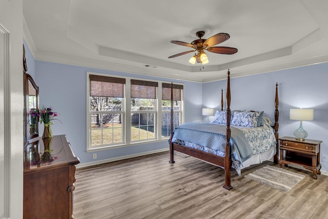 bedroom featuring light wood-type flooring, a tray ceiling, visible vents, and baseboards