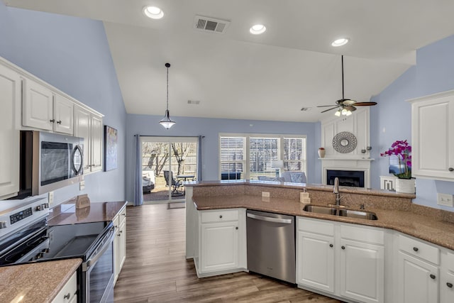 kitchen featuring a fireplace, stainless steel appliances, visible vents, a sink, and wood finished floors