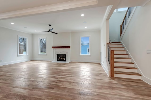 unfurnished living room with a fireplace with flush hearth, ceiling fan, light wood-type flooring, baseboards, and stairs