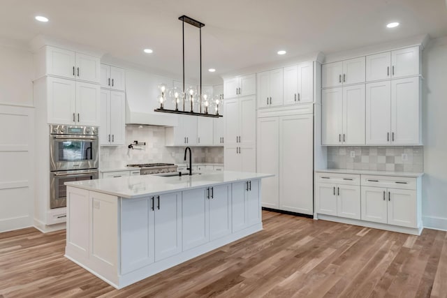 kitchen with double oven, white cabinetry, light countertops, and a sink