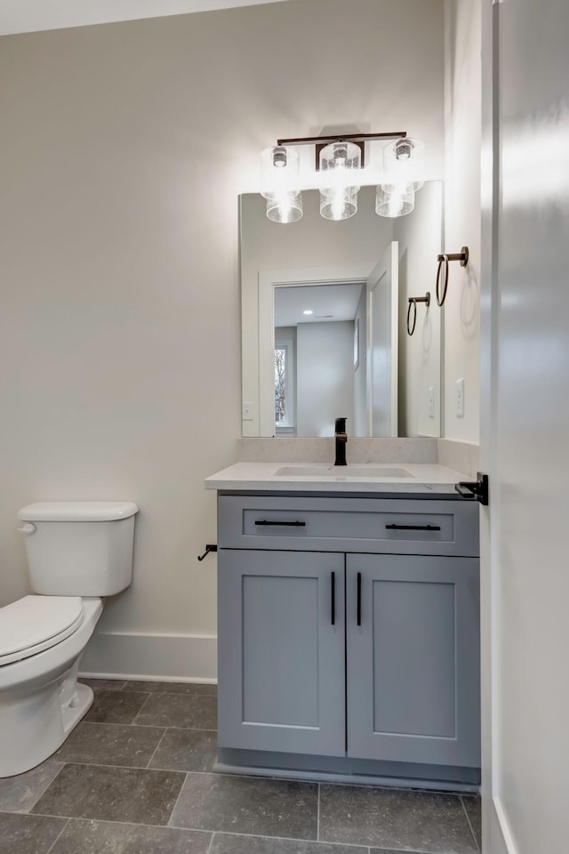 bathroom featuring stone finish flooring, toilet, vanity, and baseboards