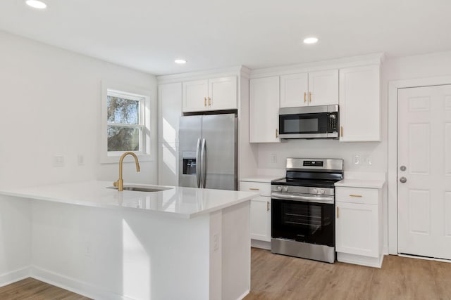 kitchen with appliances with stainless steel finishes, light countertops, light wood-type flooring, white cabinetry, and a sink