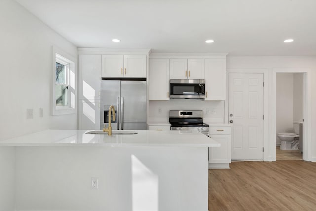 kitchen with light countertops, light wood-style flooring, appliances with stainless steel finishes, white cabinets, and a sink