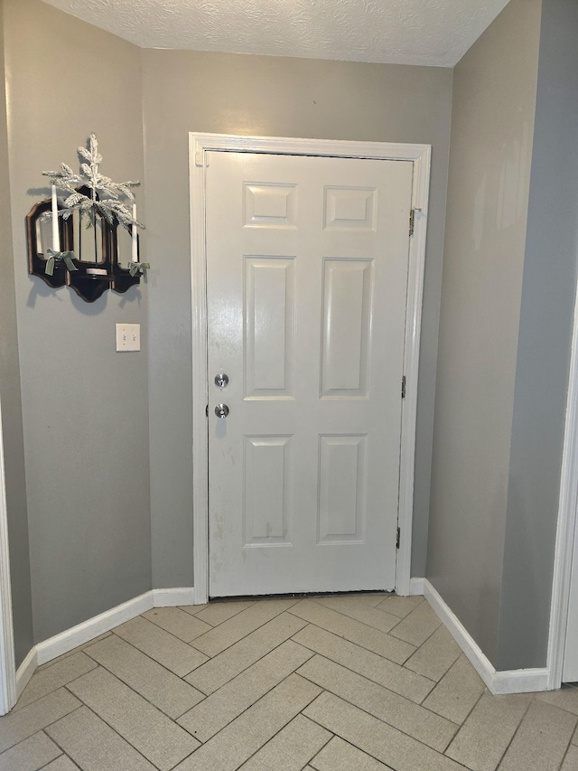 doorway to outside featuring light wood finished floors, baseboards, and a textured ceiling