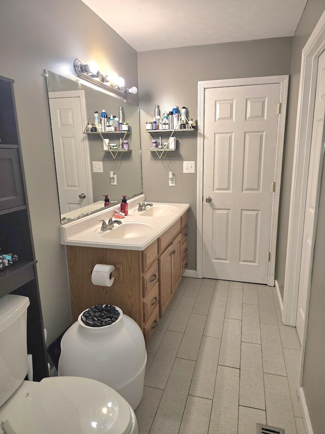 bathroom with baseboards, a sink, toilet, and double vanity