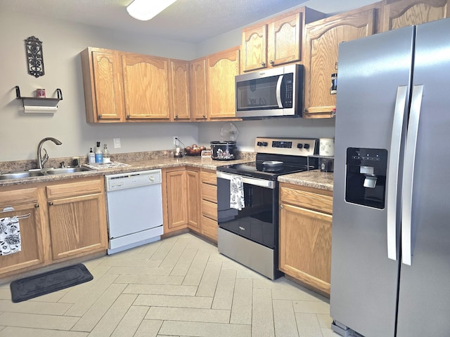 kitchen with appliances with stainless steel finishes, a sink, and light brown cabinetry